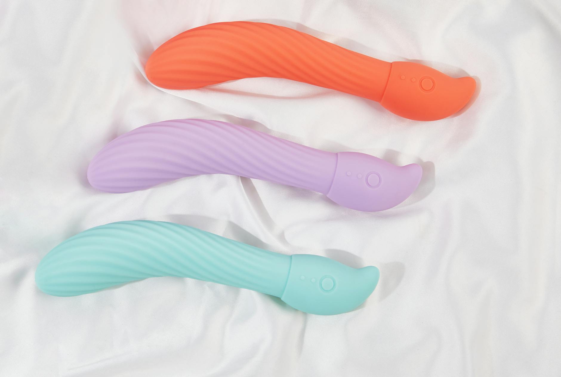 Assortment of colorful silicone clitoral vibrators and lemon vibrators on dark fabric