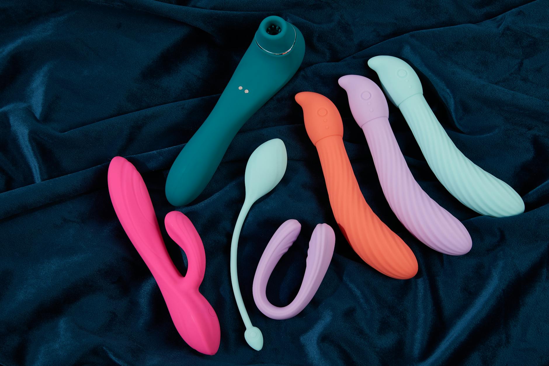 Collection of colorful silicone vibrators on dark fabric showcasing modern clitoral stimulation tools