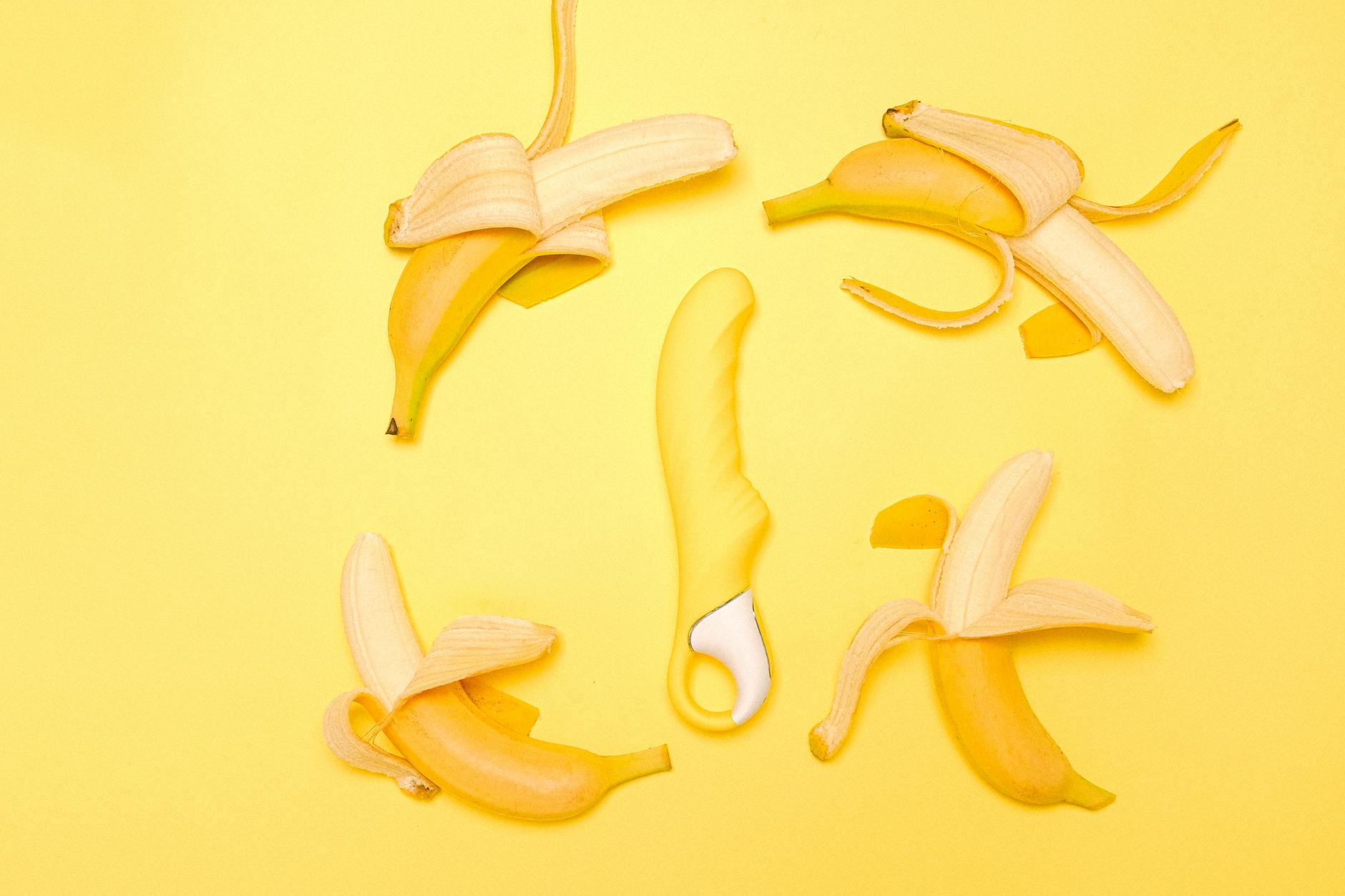 A yellow lemon vibrator on a bright yellow background surrounded by fresh lemons