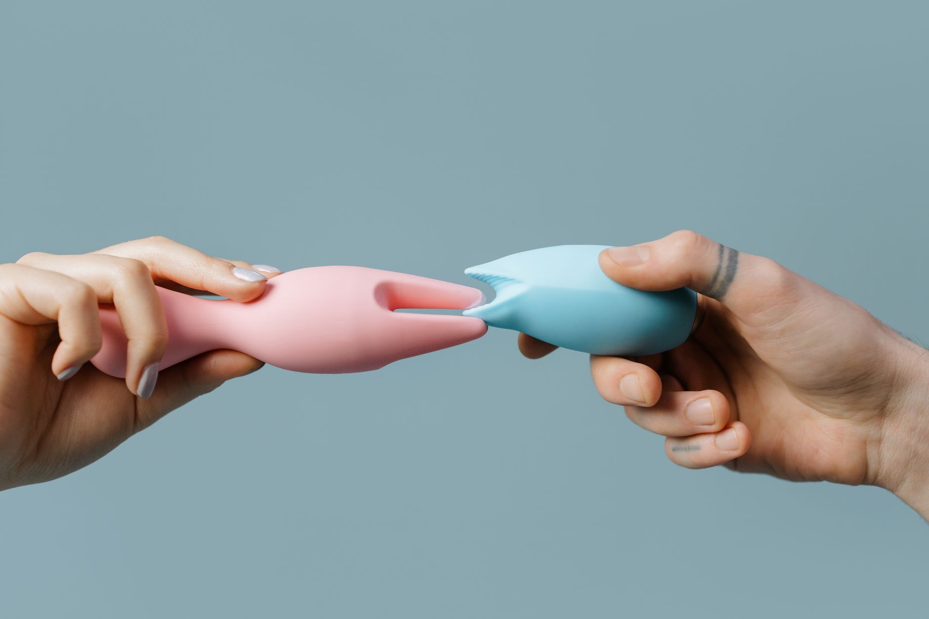 Hands holding pastel-colored silicone clitoral vibrators on a soft background