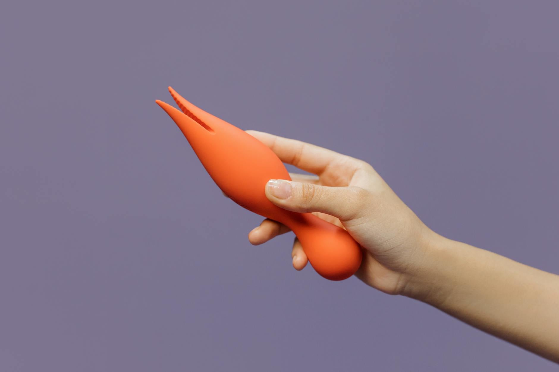 Close-up of a hand holding a lemon-colored vibrator against a minimalistic purple backdrop, showcasing modern sensuality.