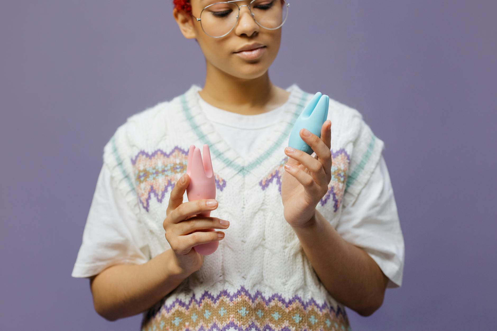 Person holding blue and pink silicone vibrators with a contemplative expression